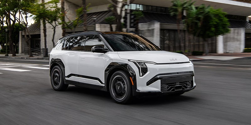 A white 2027 Kia EV3 compact electric SUV in motion on a city street.